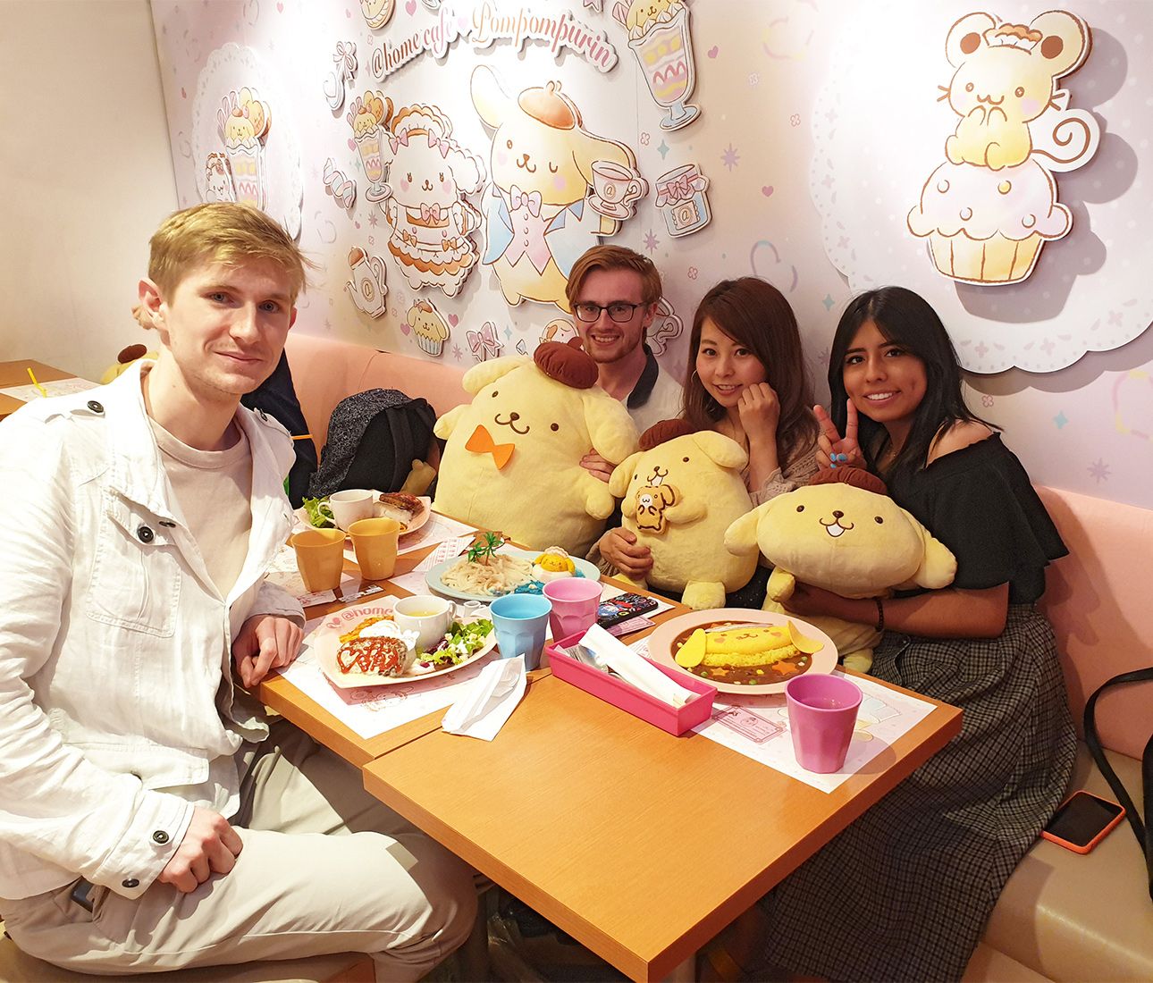 Language students sit around a table in a maid cafe cuddling big soft toys