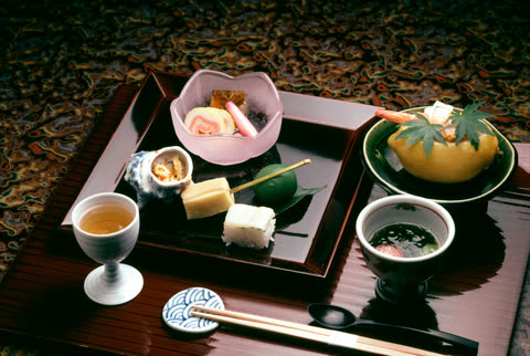 A variety of small Japanese dishes, including seafood, soup, and rice, are arranged on a dark lacquer tray.