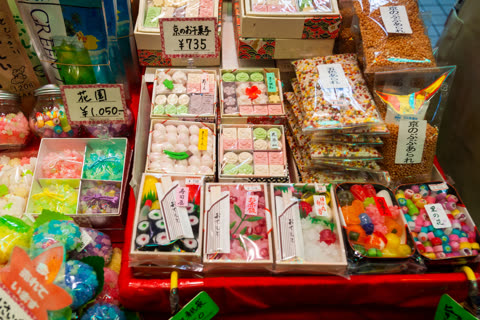 A variety of colorful, packaged Japanese candies and confections are displayed for sale on a red-covered table.