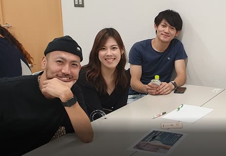 Two men and a woman sit side-by-side at a table in a room, smiling toward the camera.