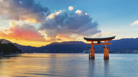 Orange torii gate stands in water at sunset, mountains in background.