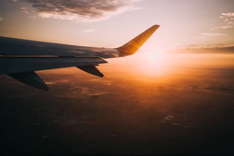 Airplane wing viewed from inside the cabin during sunset over land.