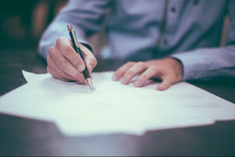 Person writing with a pen on papers at a desk.