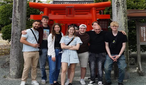 A group of eight people pose for a photo between two stone pillars in front of an orange Japanese torii gate.