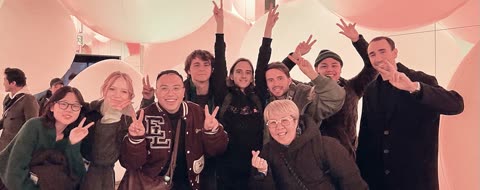 A group of people smiles and makes peace signs while posing in a room filled with large, pink inflatable orbs.