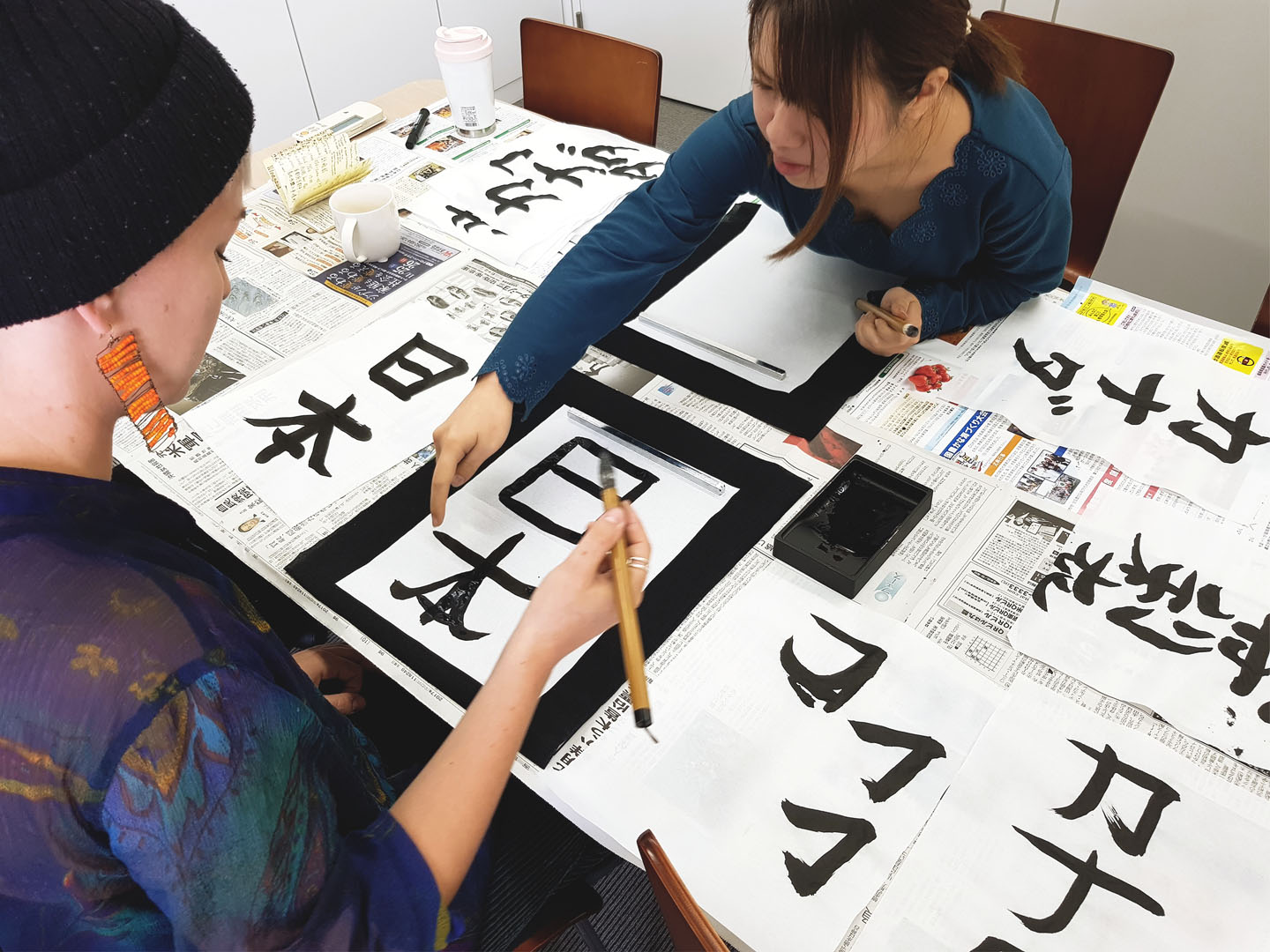 Two language students drawing japanese kanji with traditional ink